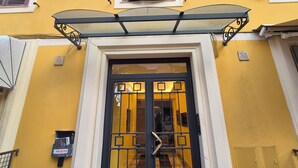 A yellow building with a black door, white shutters, and a small awning above the door. - Apartment Fiore is big, romantic,  green terrace close Trastevere and Vatican (Rome)