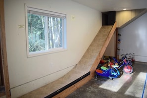 Una habitación con ventana, una escalera de madera y bicicletas infantiles.