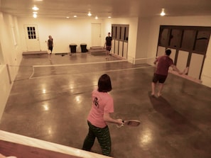 Una cancha de tenis con jugadores, una red y una puerta al fondo.