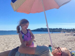 A beach scene with a person lying on a beach towel under a beach umbrella.