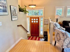 Un escalier en bois mène à une porte ornée d’un panneau de verre rouge, un canapé à motifs et un panneau affichant les règles de la maison, fixé au mur.
