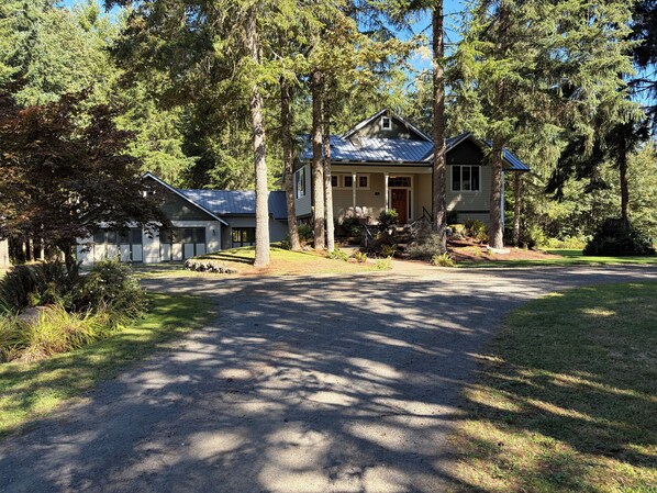 A two-story house with a front porch, surrounded by trees and a driveway.