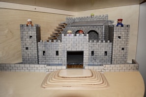 Un modelo de castillo con cuatro torres, una entrada central y una plataforma de madera al frente.