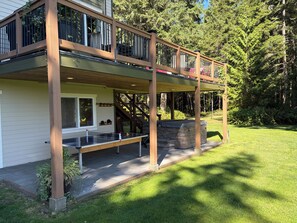 Une maison à deux étages dotée d’un patio couvert, d’une cheminée en pierre et offrant une vue sur une zone boisée.