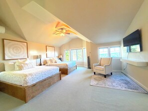 A bedroom with two beds, a ceiling fan, a mounted TV, and large windows.