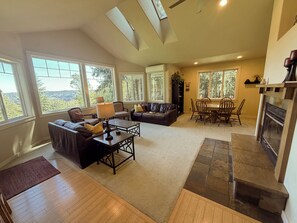 A spacious living room with a fireplace, a dining area, and large windows offering a view of the outdoors.