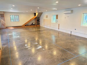 A spacious room with a polished concrete floor, a wooden staircase, and a large window providing natural light.