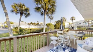 A deck with outdoor furniture, palm trees, and a view of a residential area.