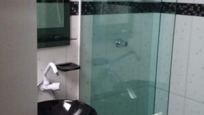 Un baño con cabina de ducha de vidrio, un lavabo negro y un espejo encima.