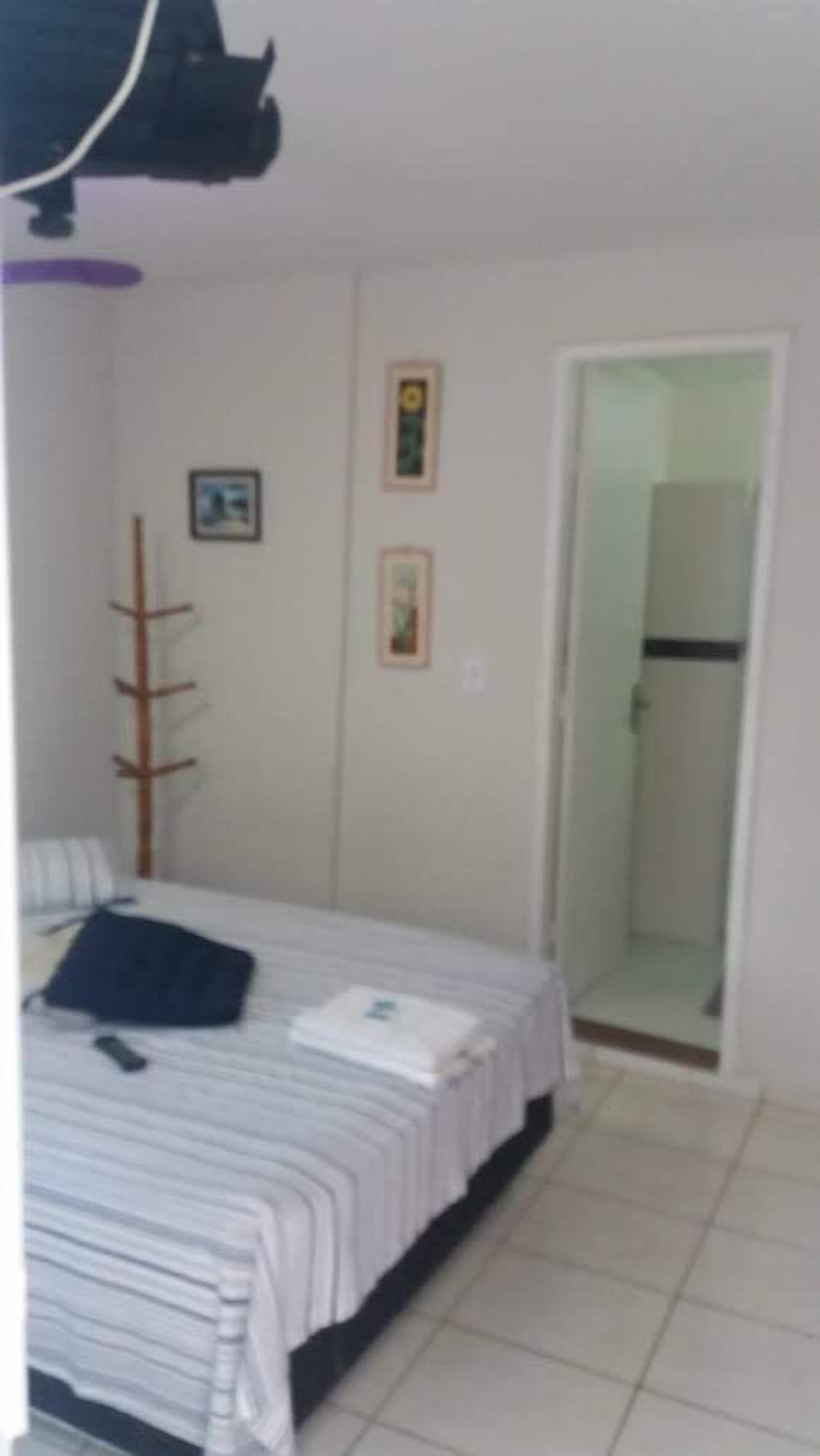 A bedroom with a bed, a bedside table, a chair, a door, and a wall-mounted shelf.