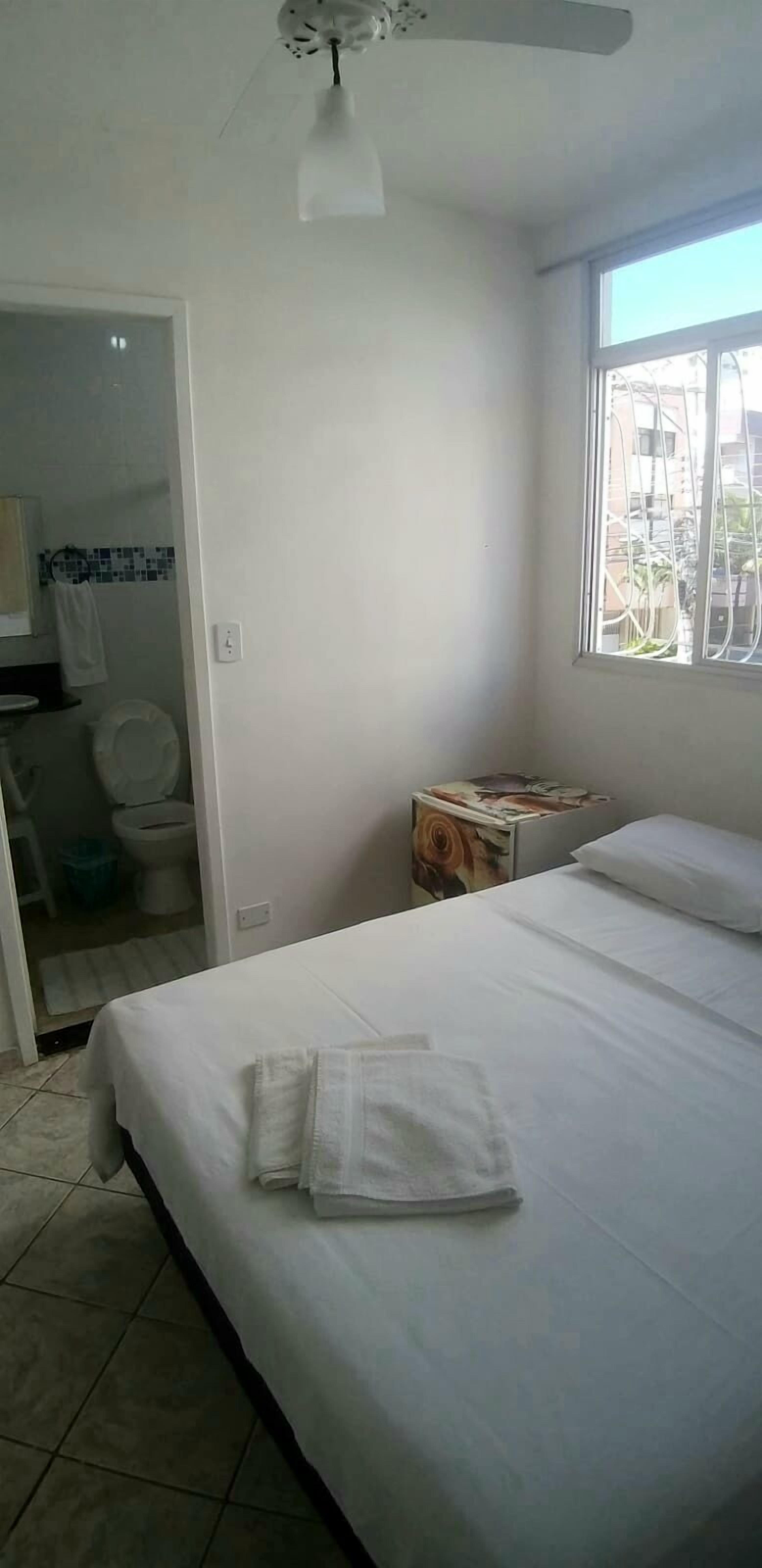 A hotel room with a bed, a bedside table, a window, and a bathroom visible through an open door.