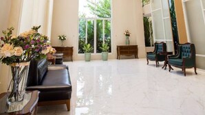 Un'ampia hall con soffitto alto, un lampadario, una zona salotto con divani e un'ampia finestra che offre vista sul verde circostante.