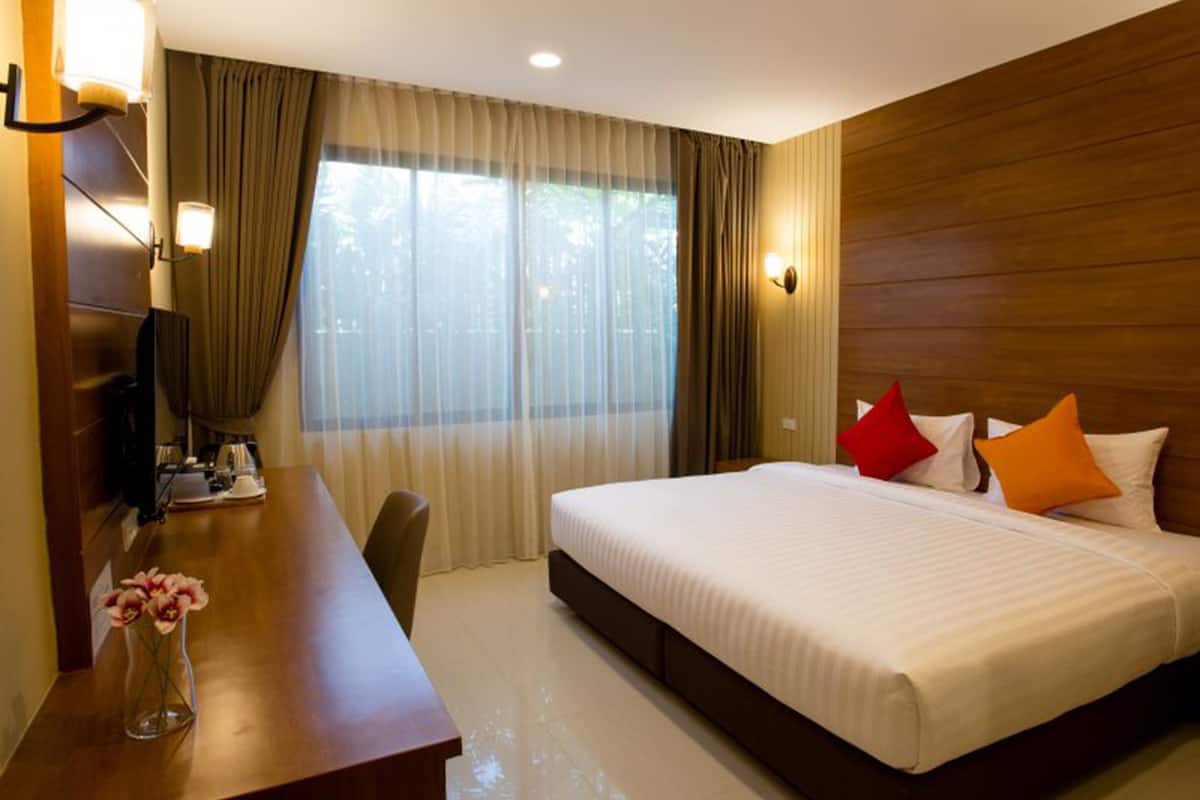 Hotelkamer met een groot bed, een bureau met stoel, een televisie en een raam met gordijnen.
