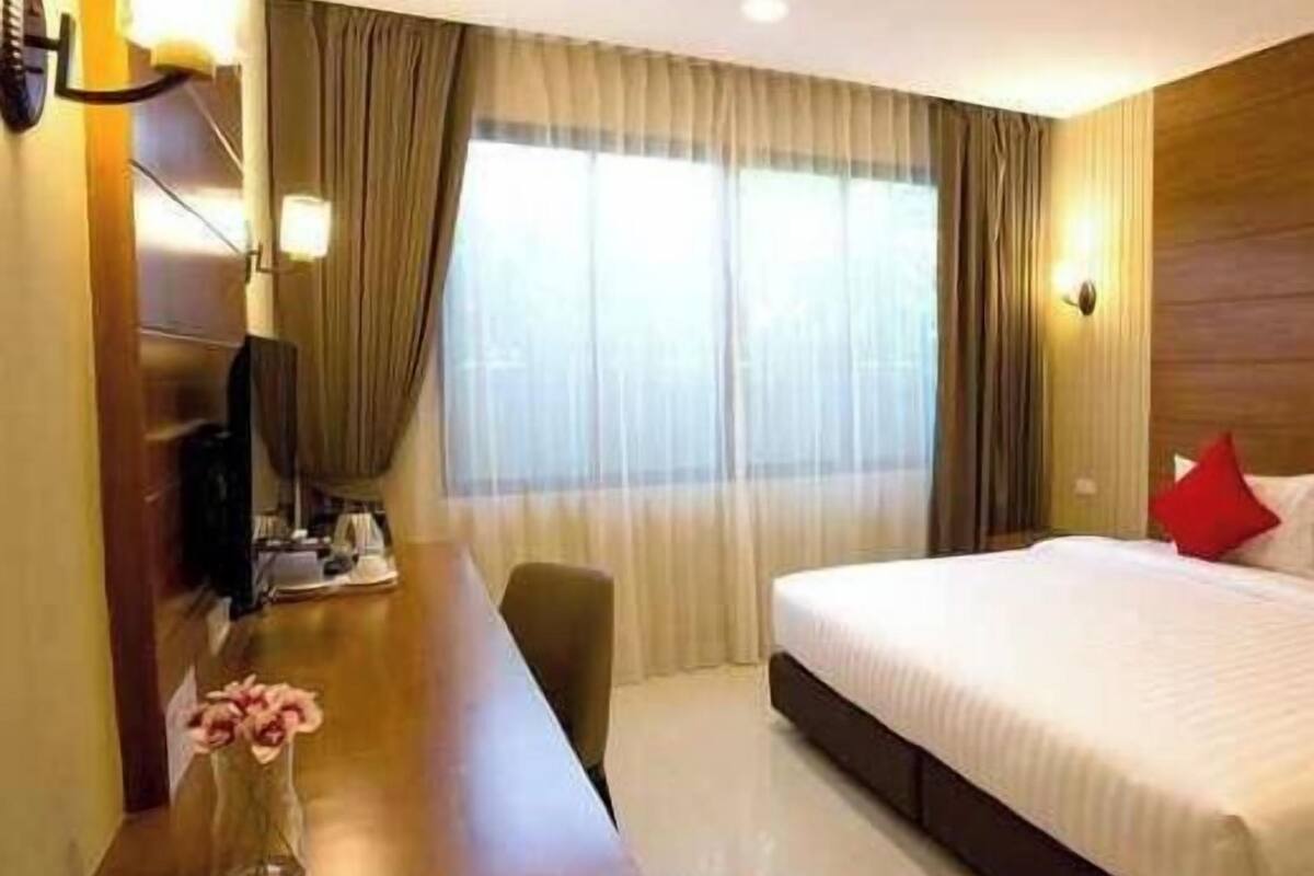 Een hotelkamer met een bed, een bureau, een stoel, een televisie en een raam met gordijnen.