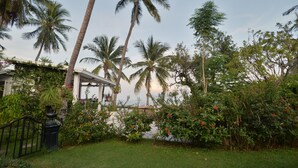 A lush garden with palm trees, a gazebo, and a view of the sea. - The Hen Hua Hin Private Beach Villa (Hua Hin)