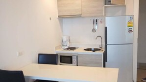 A compact kitchen with a white countertop, a built-in microwave, a coffee maker, and a refrigerator. - Acqua Condominium (Pattaya)