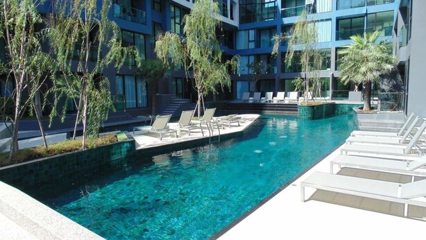 A modern hotel with a clear blue pool surrounded by lounge chairs and palm trees. - Acqua Condominium (Pattaya)