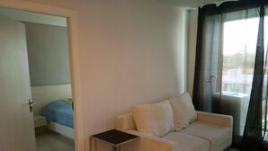 A modern living room with a white sofa, a small side table, and a door leading to another room. - Acqua Condominium (Pattaya)