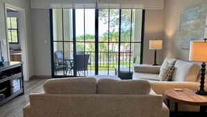 A living room with a sofa, a coffee table, and a TV stand. There is a balcony with a table and chairs. - Pacifico Paradise Condo, Playas del Coco, Guanacaste, Costa Rica (Coco)