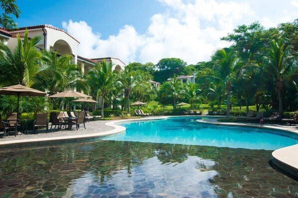 Una piscina de resort rodeada de palmeras y sillas de descanso.