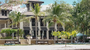 A multi-story building with a modern architectural style, featuring balconies, large windows, and a central courtyard with seating areas and palm trees. - Pacifico Paradise Condo, Playas del Coco, Guanacaste, Costa Rica (Coco)