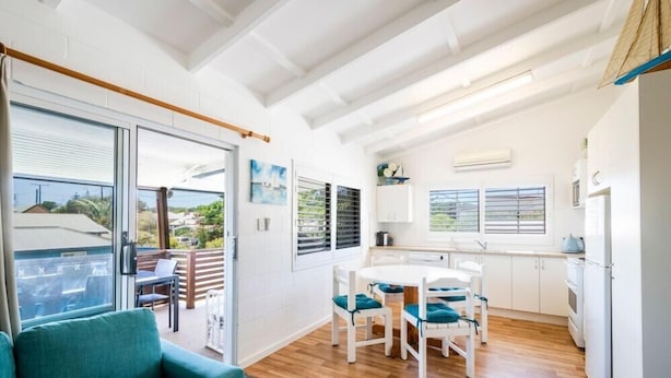 A modern kitchen with white cabinets, a dining area with a round table and chairs, and a balcony with a sofa. - Captains Bridge Wooli (Wooli)