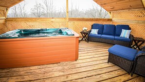 Eine Holzterrasse mit Whirlpool, blauen gepolsterten Sitzgelegenheiten und Korbmöbeln.