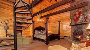 Ein Blockhaus-Interieur mit Wendeltreppe, einem Himmelbett, einem Kamin aus Stein und einer gemütlichen Sitzecke.
