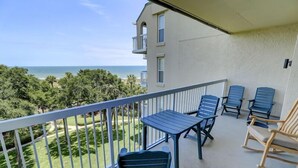 A balcony with a table and chairs, overlooking a beach and greenery. - Fully Updated Kitchen and Bathrooms with an Ocean View! (Hilton Head)