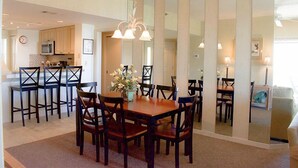 A dining area with a wooden table and chairs, a flower vase, and a kitchen in the background. - Fully Updated Kitchen and Bathrooms with an Ocean View! (Hilton Head)