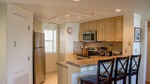 A kitchen with a central island, wooden cabinets, a microwave, and a refrigerator. - Fully Updated Kitchen and Bathrooms with an Ocean View! (Hilton Head)