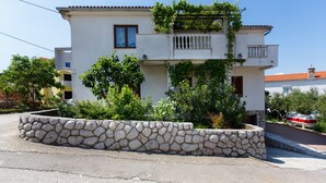 A two-story building with a stone retaining wall in front, a balcony with climbing plants, and a red-tiled roof. - JP1 - apartman for 2 (Vrbnik)