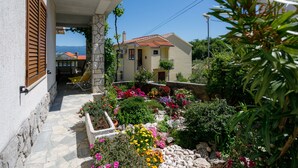 A house with a stone facade, a tiled roof, and a garden with various plants and flowers. - JP1 - apartman for 2 (Vrbnik)