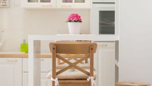 A kitchen with white cabinets, a wooden chair with a cushion, and a small stool.