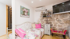 A bedroom with a bed, a nightstand, a bench, a painting, and a stone wall.