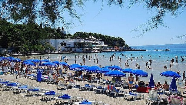 A beach with numerous blue umbrellas and sun loungers.
