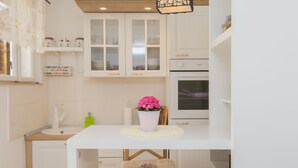 A kitchen with white cabinets, a white countertop, a white table, and a chair with a cushion.