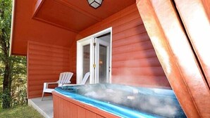 Eine Holzhütte mit Whirlpool auf der Veranda, einer Tür und einem Stuhl.