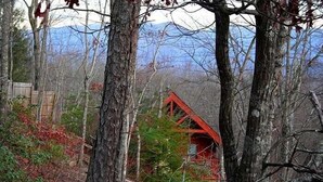 Eine Hütte mit rotem Dach, umgeben von Bäumen und einem Berg im Hintergrund.