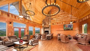 Amplia sala de estar con chimenea, techo de madera y ventanas grandes que ofrecen vistas a la montaña.