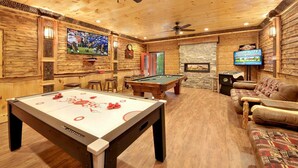 Una sala de recreación interior acogedora con mesa de billar, mesa de fútbol de mesa, zona de estar cómoda y televisor mostrando un partido deportivo.