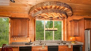 Cocina de cabaña de madera con una ventana grande, armarios de madera, encimeras de granito y una lámpara colgante.