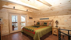 Une chambre aménagée dans une cabane en bois, avec un lit, des tables de chevet, une fenêtre et une porte donnant sur l’extérieur.
