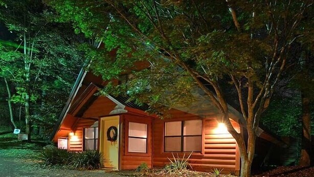 Une cabane avec un toit en pente, un porche à l’avant et une porte ornée d’une guirlande.