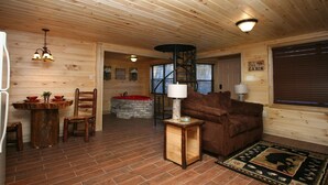 L’intérieur d’un chalet en bois comprend une table à manger, des chaises, un canapé, une lampe, une cheminée et une fenêtre avec des stores.