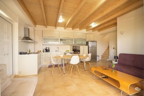 A modern kitchen with white cabinets, a wooden dining table, and a purple sofa.