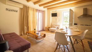 Una sala moderna con sofá, un banco de madera, una mesa de comedor con sillas y una zona de cocina con estufa y armarios.