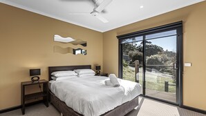 Une chambre dotée d’un grand lit, d’un ventilateur de plafond, d’une table de chevet avec une lampe, d’une fenêtre donnant sur un paysage verdoyant et d’une porte-fenêtre coulissante.