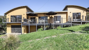Une maison moderne à deux étages, dotée d’un balcon, de grandes fenêtres et de parasols d’extérieur.