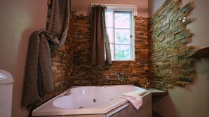 Un baño con pared de piedra, una ventana, una bañera y una toalla colgada en la pared.